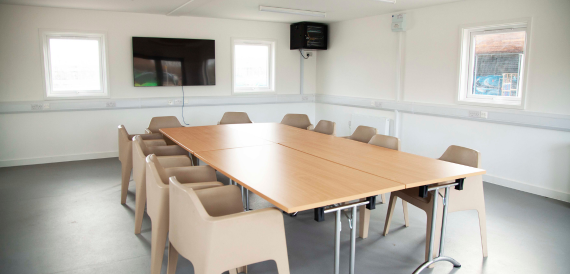 Meeting room with a wooden table, cream chairs and a wall-mounted screen