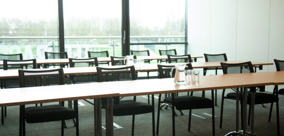 Classroom-style meeting room with rows of tables facing floor-to-ceiling windows