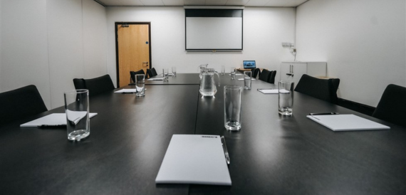Boardroom table set with water glasses, notepads and a projector screen