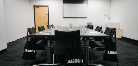 Meeting room with black chairs, Barbican branded bags and a projector screen