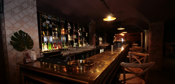 Bar counter lined with shelves of spirits under warm lighting