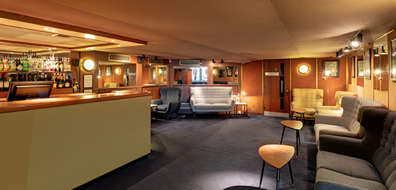 Bar lounge with a mustard sofa, wooden stool and wall lights