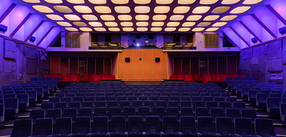 Retro auditorium with a honeycomb ceiling, blue seats and a red-curtained stage