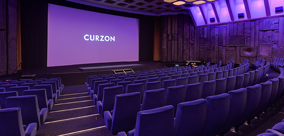 Cinema auditorium with purple-blue seats facing an illuminated Curzon screen