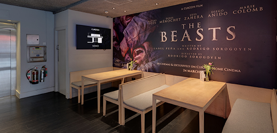 Cafe with wooden tables and bench seating below a film poster