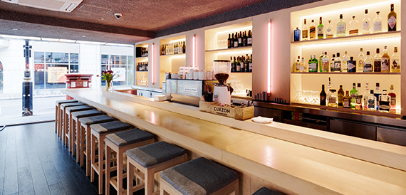 Wooden bar counter with high stools and shelves of bottles