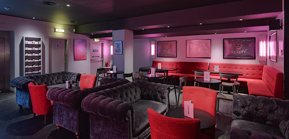 Lounge with pink lighting, red banquette seating and a staircase