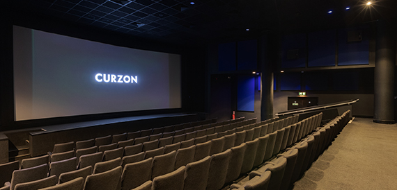 Cinema auditorium with grey seats facing an illuminated Curzon screen