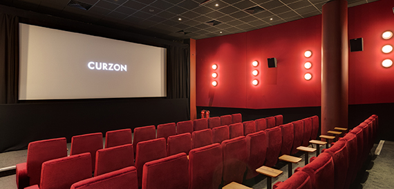Cinema auditorium with red seats and a row of wall-mounted lights