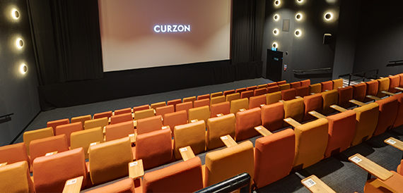Cinema auditorium with orange velvet seats facing an illuminated Curzon screen