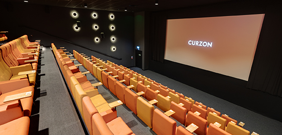 Cinema auditorium with orange seats facing an illuminated Curzon screen
