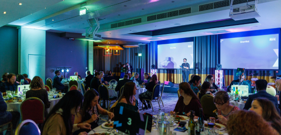 Awards dinner with guests seated at tables facing two large presentation screens