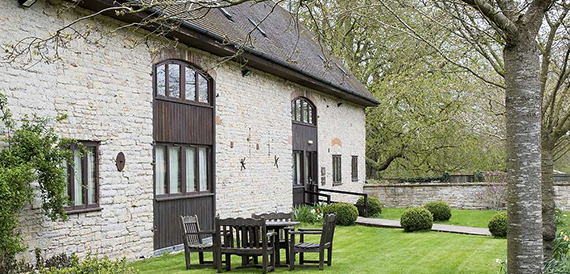 Stone courtyard exterior with a wooden table, chairs and lawn