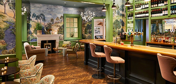 Green-painted bar with a mural, wooden floor and leather stools