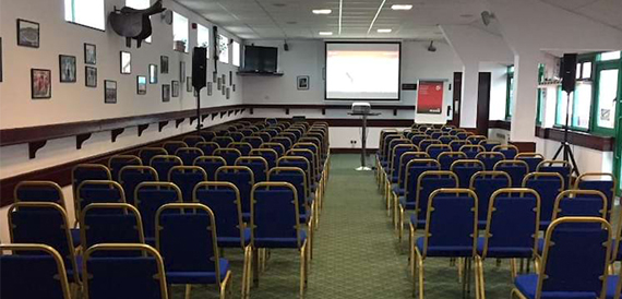 Meeting room with rows of blue chairs facing a screen and photos
