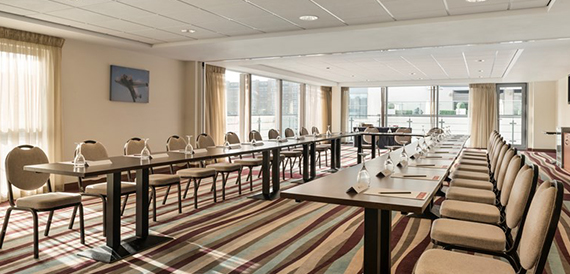 Meeting room set boardroom-style with rows of tables on striped carpet