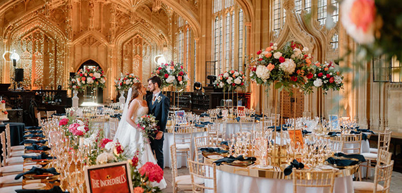 Bride and groom embracing beneath a floral arch in a gothic hall