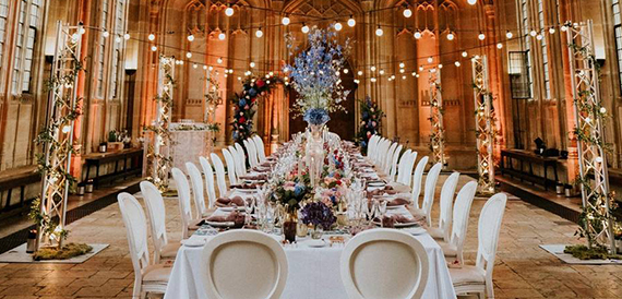 Long banquet table lit by festoon lights beneath a floral archway