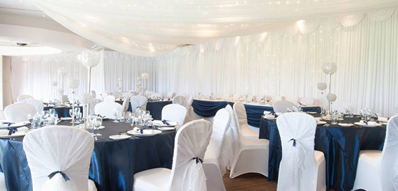 Round tables with navy chair sashes set beneath draped white fabric