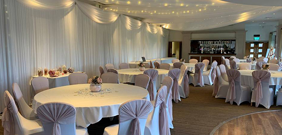 Round tables dressed in white with silver sashes beneath a fairy-lit canopy