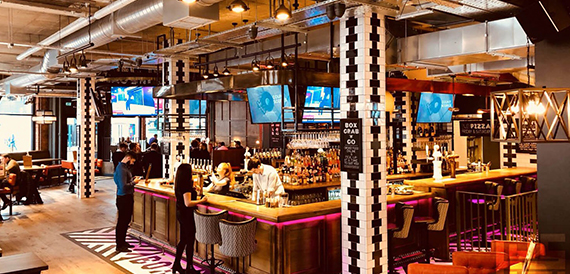 Bartenders serving customers at a busy bar lit with pink floor lighting
