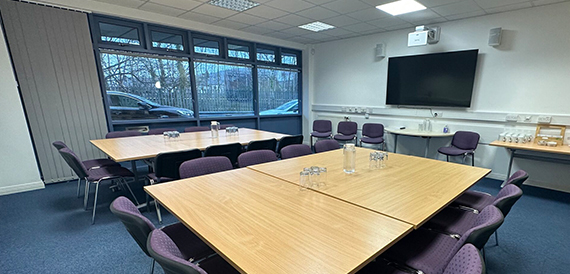 Meeting room with tables in an L-shape, purple chairs and windows overlooking the car park