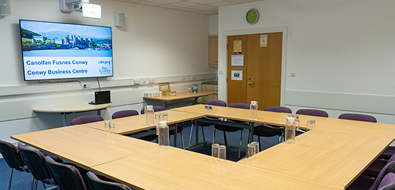 Boardroom tables arranged in a square set beneath a branded welcome screen