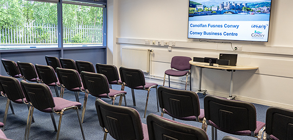 Rows of purple chairs facing a screen displaying Conwy Business Centre branding