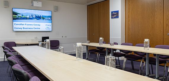 Meeting room with two rows of tables and purple chairs facing a wall screen