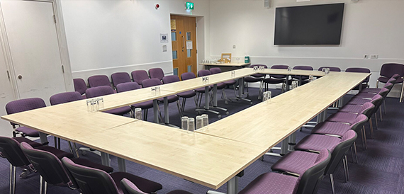 Meeting room with tables arranged in a U-shape and purple chairs
