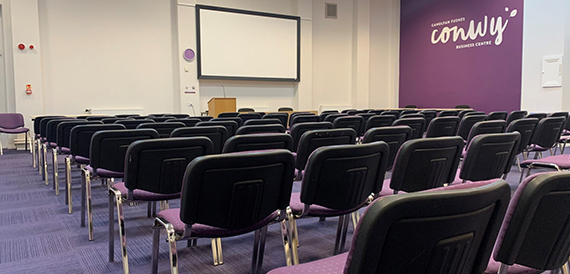 Conference room set theatre-style with purple chairs facing a projector screen