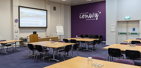 Classroom-style meeting room with a purple accent wall and Conwy Business Centre branding