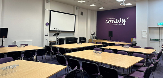 Meeting room with a whiteboard screen beside a purple accent wall bearing the Conwy logo
