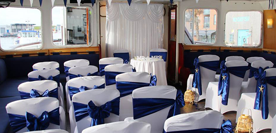 Boat function room with white chair covers and navy blue sashes set for a wedding