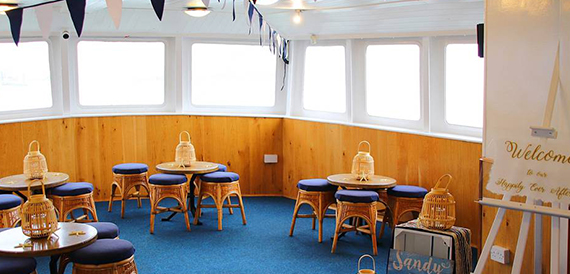 Boat lounge with wicker stools and round tables set for a celebration