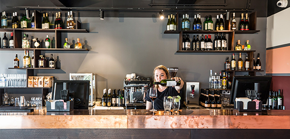 Bartender pouring a drink behind shelves of spirits and wine