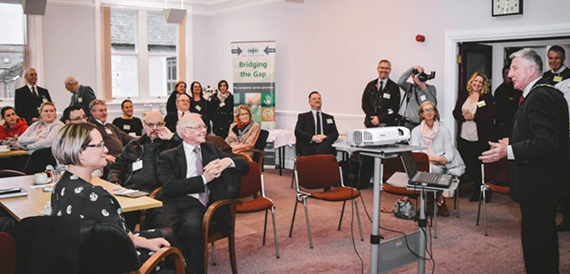 Attendees seated at an event beneath a Bridging the Gap banner and projector