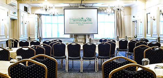 Conference room set theatre-style with blue chairs facing a County Hotel Chelmsford screen