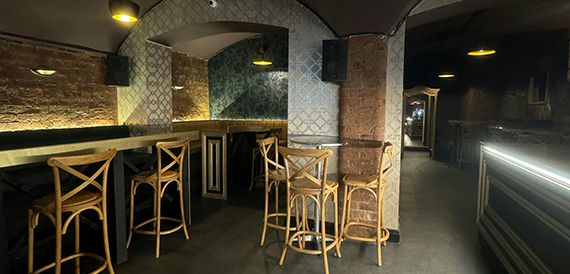 Vaulted brick seating area with wicker stools around high tables