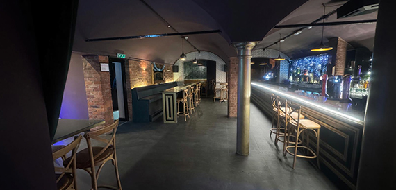 Vaulted brick bar with a long counter and wicker bar stools
