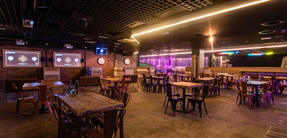 Games and bar area with dartboard screens, wooden tables and pink neon lighting