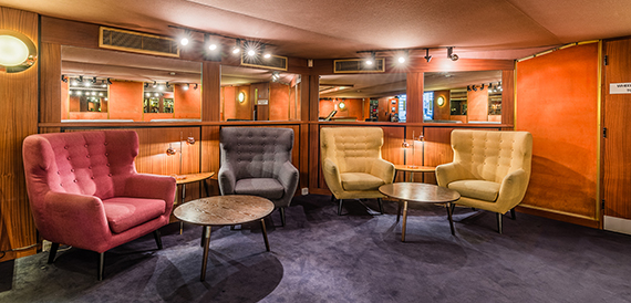 Lounge with mismatched armchairs, round tables and wood-panelled mirrored walls