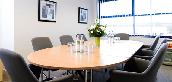 Oval boardroom table with grey chairs and water glasses set out