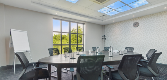 Boardroom with an oval table, black chairs and tall windows overlooking woodland
