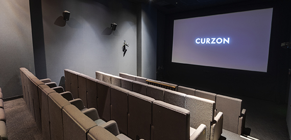 Screening room with brown seats facing an illuminated Curzon screen