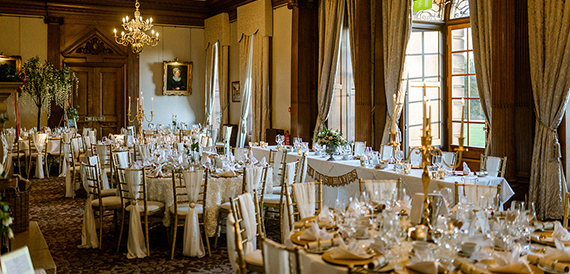 Dining room with round tables, cream chair covers and gold sashes beneath chandeliers