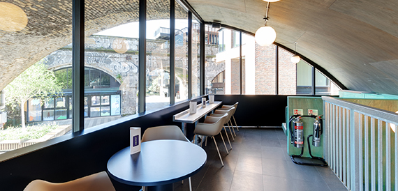 Cafe seating beside floor-to-ceiling windows overlooking brick archways