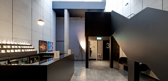 Foyer ticket counter with illuminated menu boards beside a black staircase
