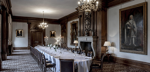 Wood-panelled dining room with a long table, dark chairs and portrait paintings