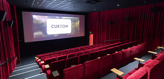 Cinema auditorium with red velvet seats facing an illuminated Curzon screen